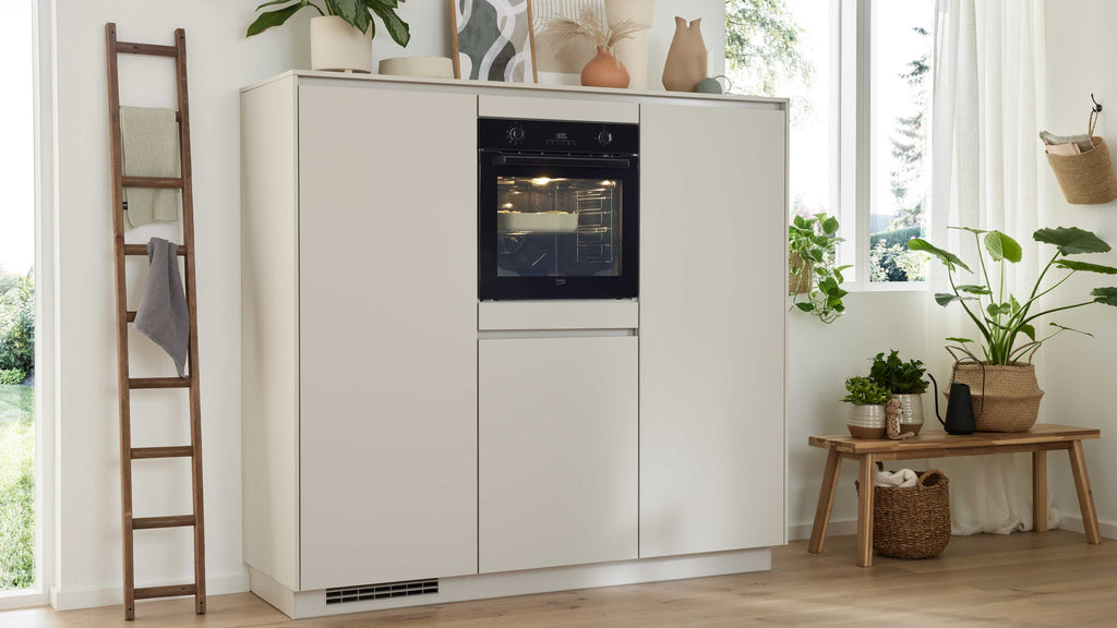 Ein heller Küchenschrank mit integriertem Backofen, daneben eine Holzleiter mit Handtüchern und eine Ablage mit Pflanzen und Körben.