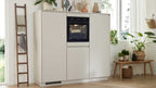 Ein heller Küchenschrank mit integriertem Backofen, daneben eine Holzleiter mit Handtüchern und eine Ablage mit Pflanzen und Körben.