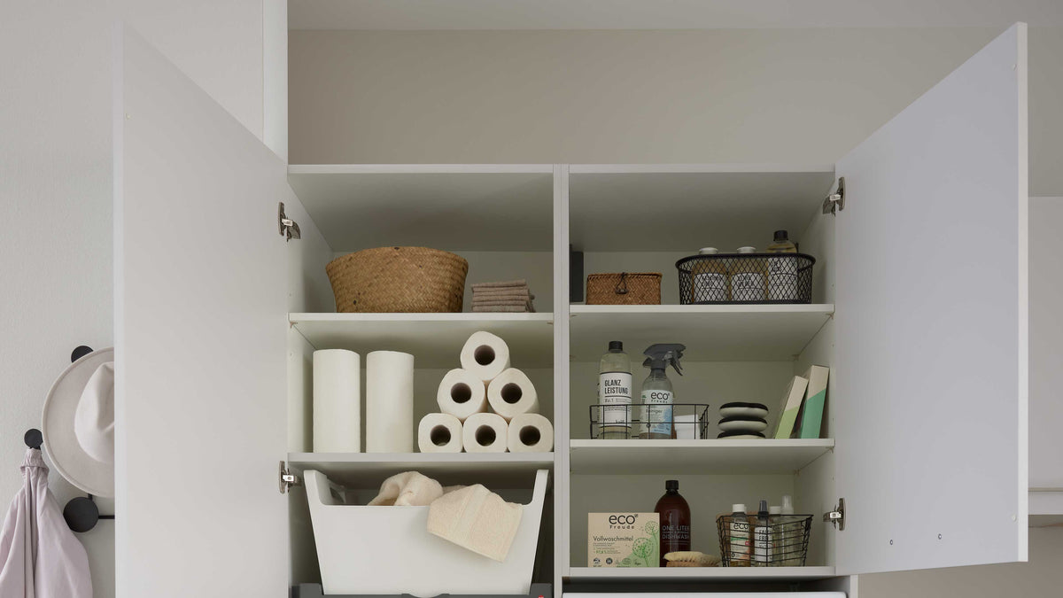 Ein weißer Schrank offen mit zwei Regalfächern, gefüllt mit Papiertüchern, Reinigungsmitteln, Handtüchern und Körben.