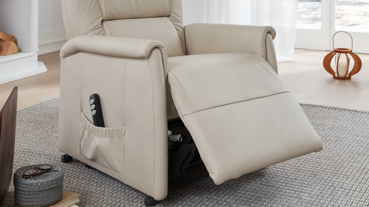 Beige Relaxsessel mit ausgeklapptem Fußteil, seitlicher Tasche für eine Fernbedienung, auf einem strukturierten Teppich.