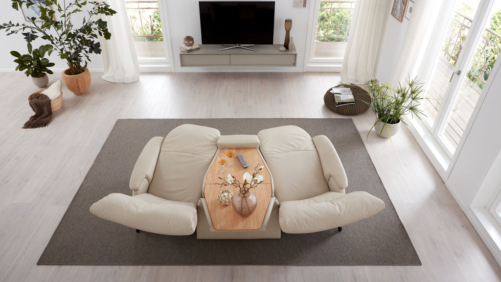Ein beiger Sofa mit zwei Einzelteilen steht auf einem grauen Teppich, im Zentrum ein hölzerner Tisch mit Dekoration.