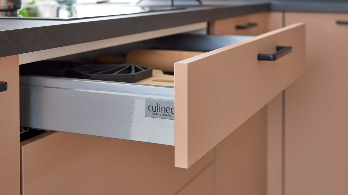 Ein offener Küchenauszug mit einem grauen Innenfach, einer Holzrolle und einem schwarzen Gadgets-Organizer, vor einer nussbaumfarbenen Front.
