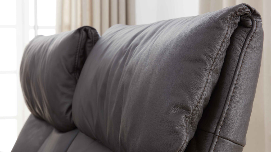 Der altgraue Kopfteil eines Polstersofas mit weichem, genarbtem Bezug und sichtbaren Nähten.