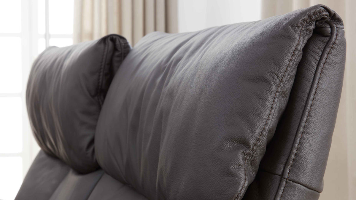 Der altgraue Kopfteil eines Polstersofas mit weichem, genarbtem Bezug und sichtbaren Nähten.