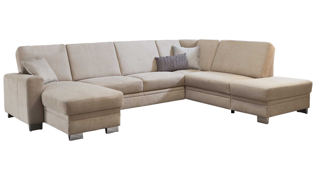 L-förmige Couch in hellem Beige mit mehreren Kissen, darunter ein dekoratives Kissen in Dunkelgrau, auf niedrigen Füßen.
