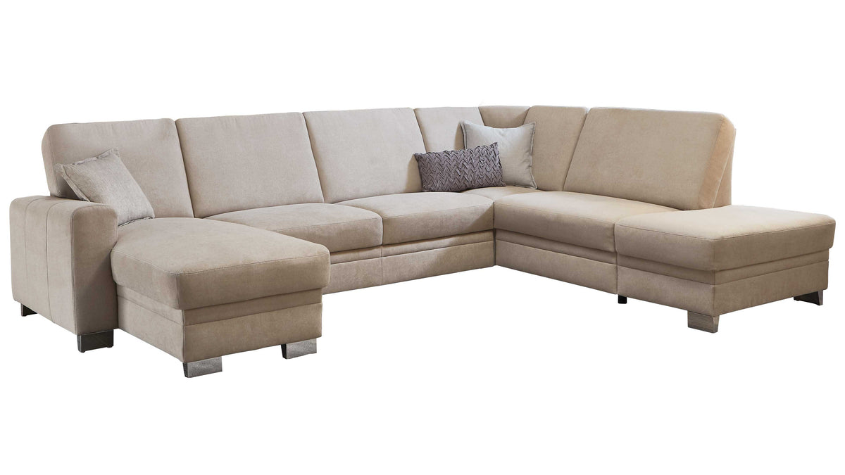 L-förmige Couch in hellem Beige mit mehreren Kissen, darunter ein dekoratives Kissen in Dunkelgrau, auf niedrigen Füßen.