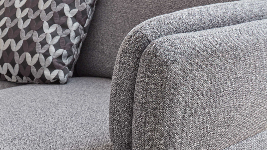 Grau gepolstertes Sofa mit abgerundeten Armlehnen und einem gemusterten Kissen in Schwarz, Weiß und Grau.