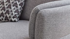 Grau gepolstertes Sofa mit abgerundeten Armlehnen und einem gemusterten Kissen in Schwarz, Weiß und Grau.