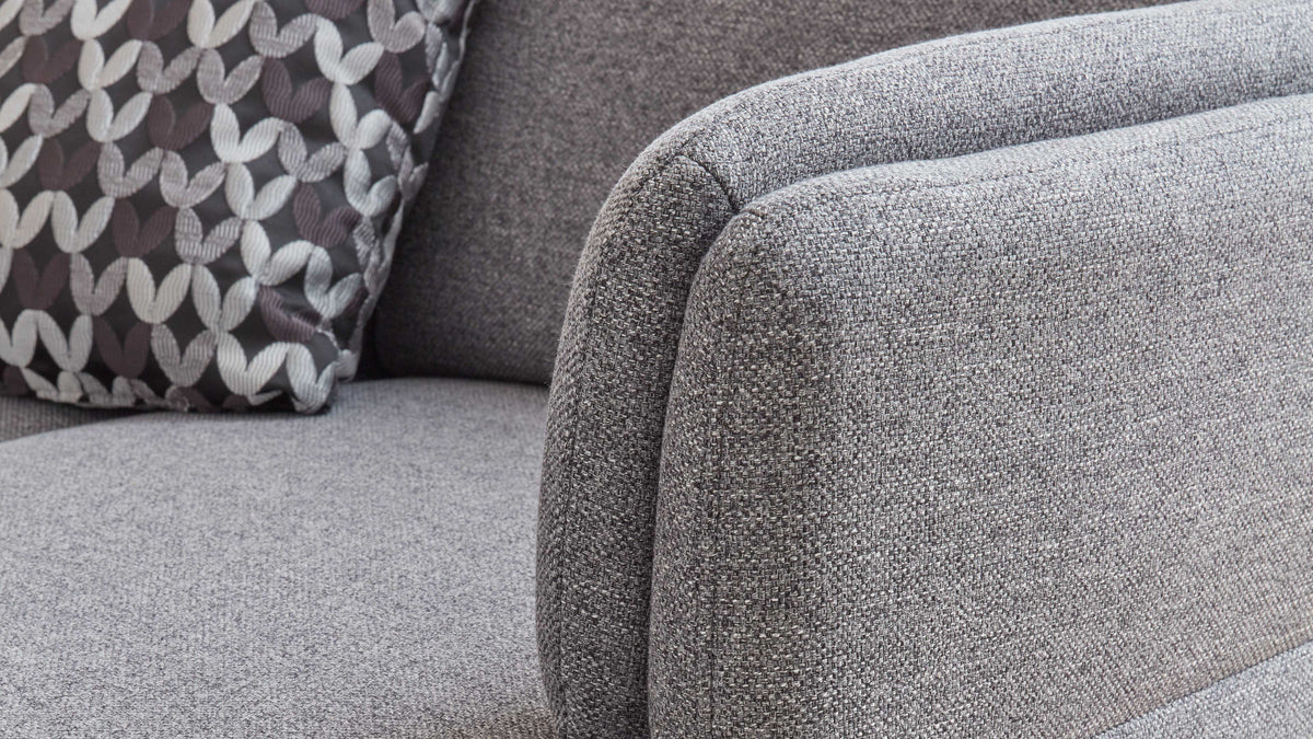 Grau gepolstertes Sofa mit abgerundeten Armlehnen und einem gemusterten Kissen in Schwarz, Weiß und Grau.