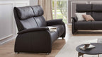 Brauner Sofa mit hohen, gepolsterten Rückenlehnen und abgerundeten Armlehnen, daneben ein kleiner runder Tisch mit Geschirr.