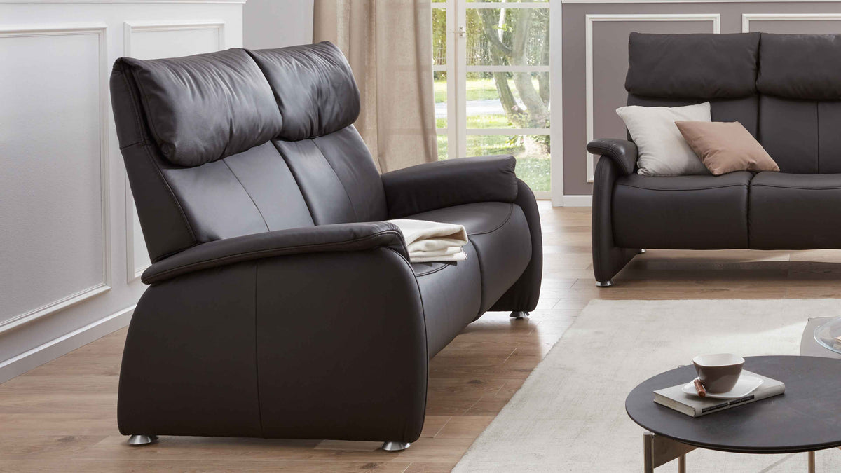 Brauner Sofa mit hohen, gepolsterten Rückenlehnen und abgerundeten Armlehnen, daneben ein kleiner runder Tisch mit Geschirr.