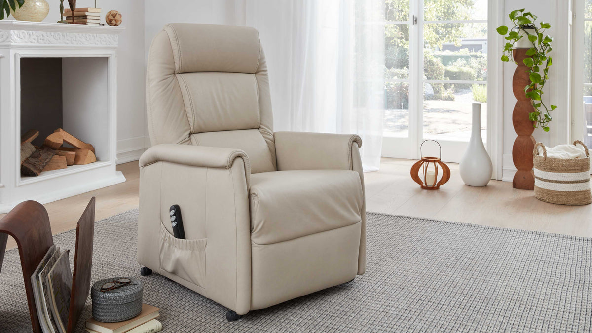 Beige Relaxsessel mit Armlehnen, einfacher Bedienung über Fernbedienung, steht auf einem hellen Teppich in einem lichtdurchfluteten Raum.