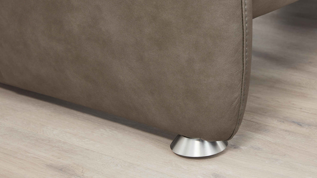 Die untere Ecke eines braunen Sofas mit einer eleganten Metallfüße ist auf einem hellen Holzboden sichtbar.